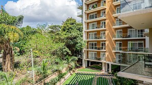 A multi-story residential building with balconies, a rooftop garden, and a well-maintained lawn.