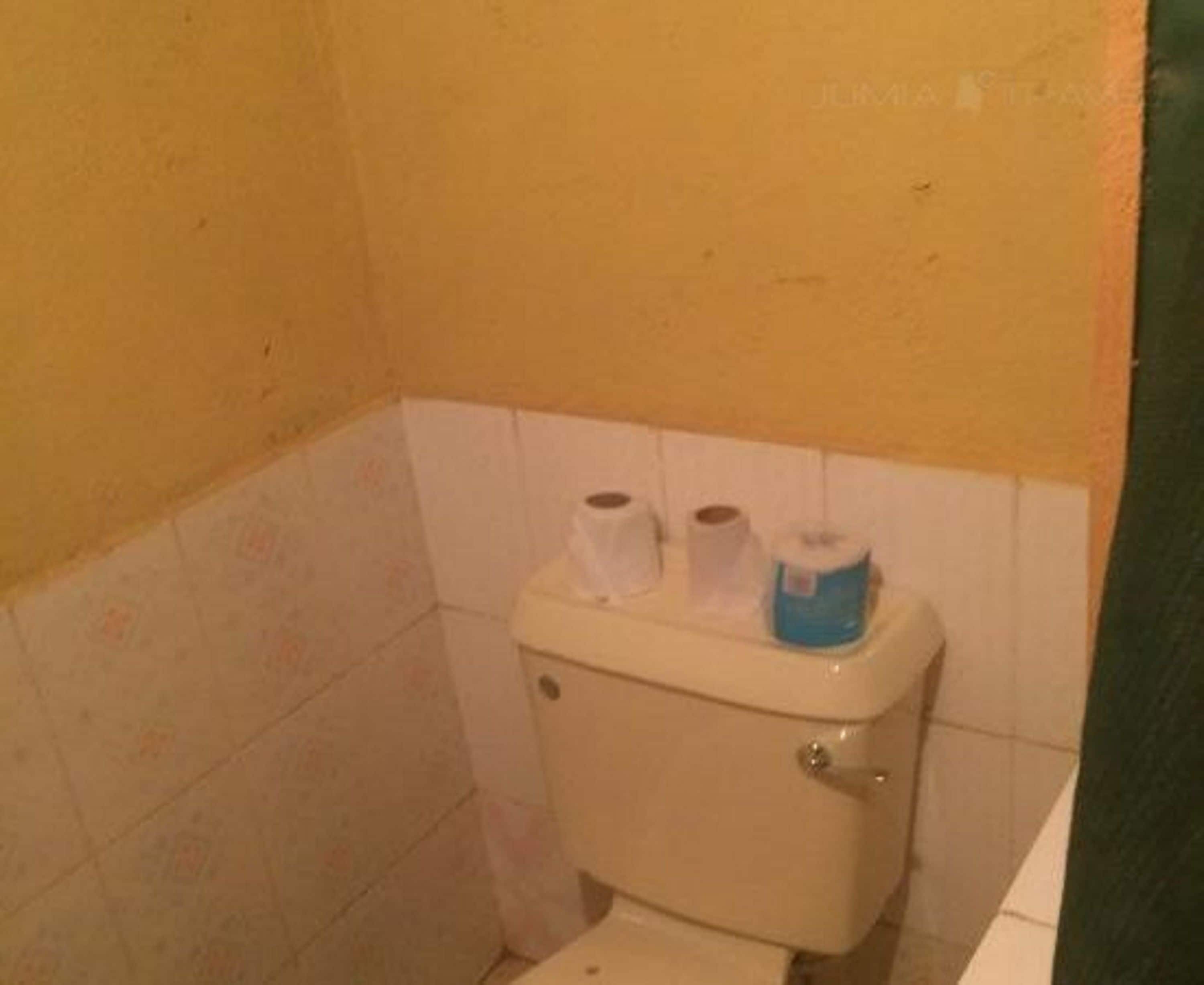 A small bathroom with a toilet, two rolls of toilet paper, and a green wall.