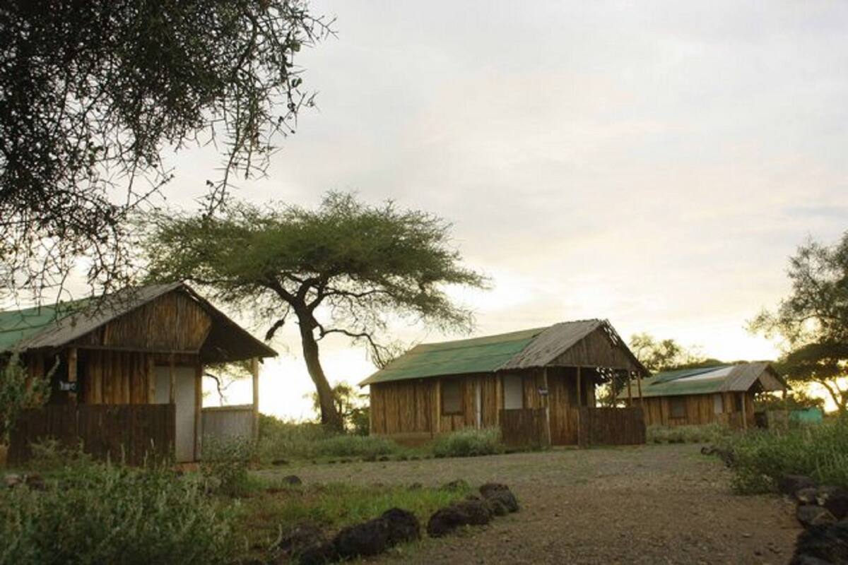 Un edificio rústico de madera con techo verde, rodeado de vegetación natural y rocas.