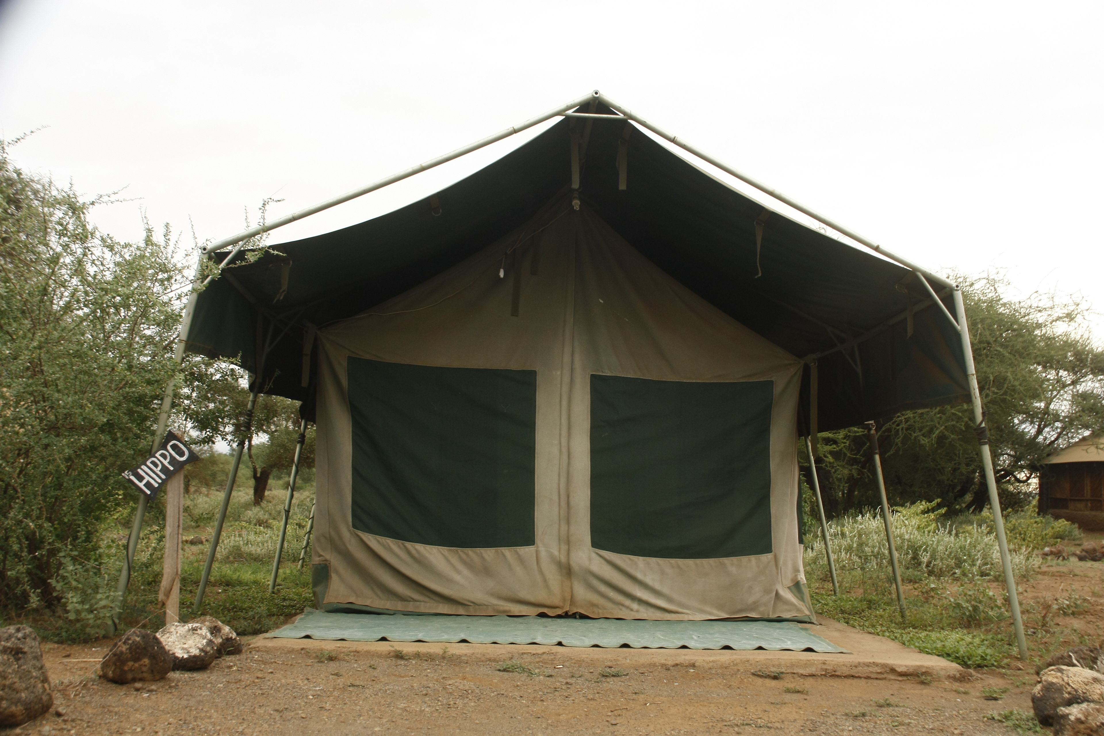 A large, enclosed tent with a green interior, set in a natural environment with rocks and vegetation around.
