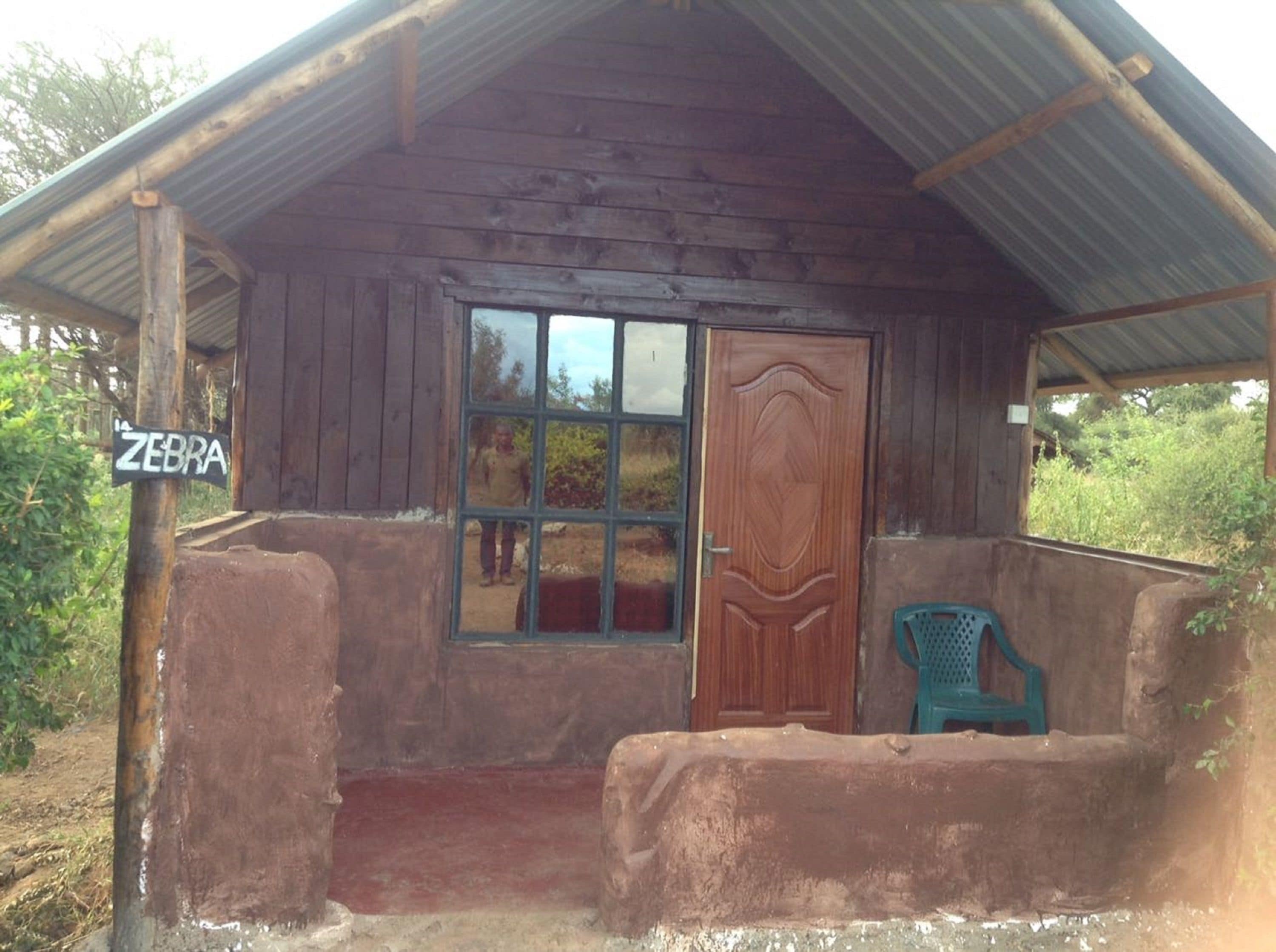 A rustic wooden cabin with a corrugated metal roof, a wooden door, and a window with a view of the surrounding landscape.