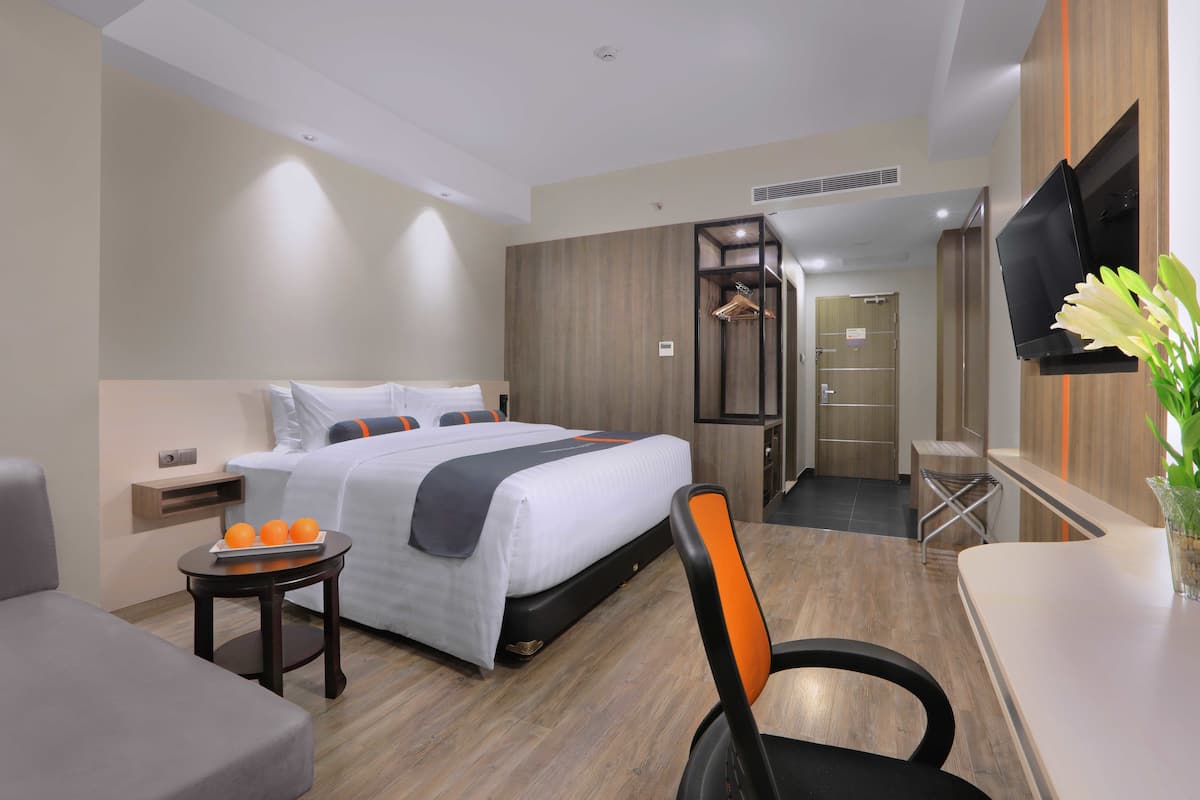 Habitación de hotel con una cama, un escritorio, una silla, una mesita con naranjas y un televisor.