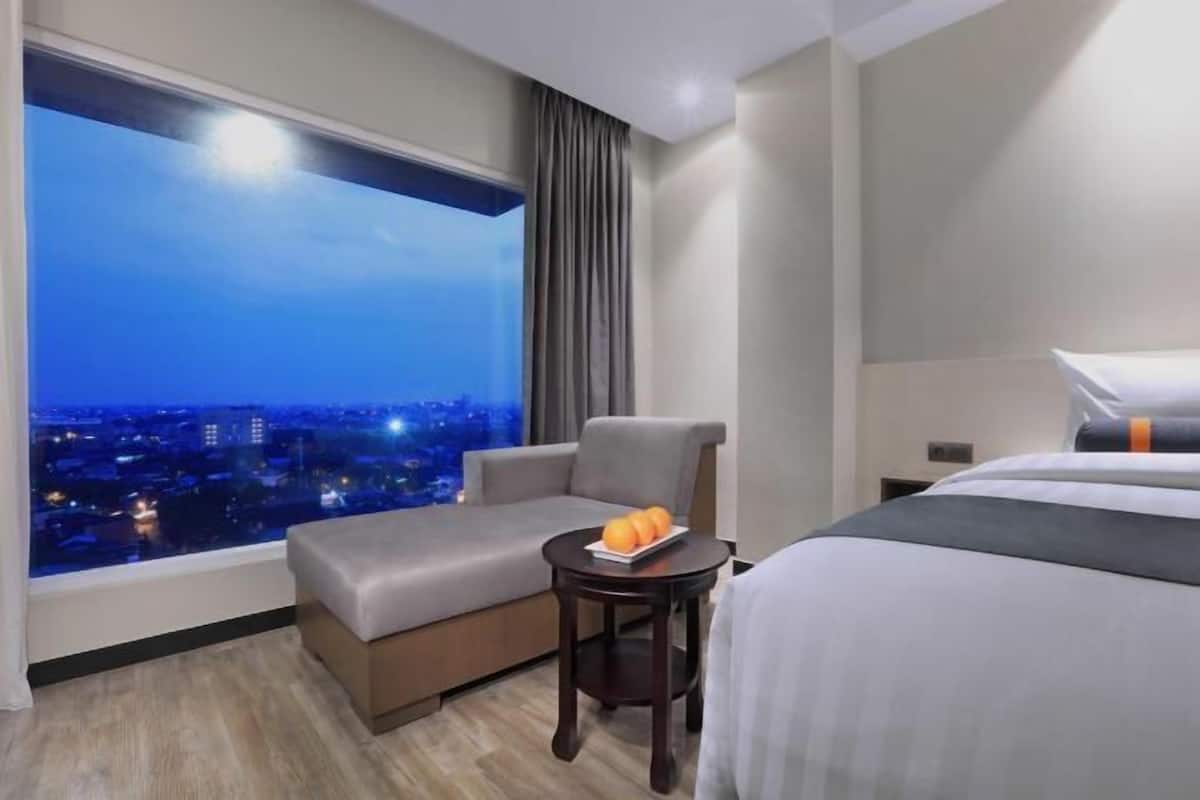 Una habitación de hotel con un ventanal grande, un sofá, una mesita con fruta y una cama.