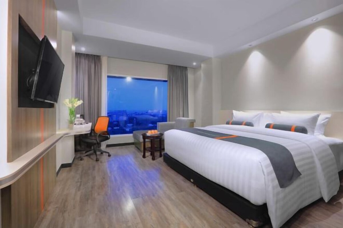 Une chambre d’hôtel équipée d’un lit, d’un bureau, d’une chaise, d’une télévision et d’une fenêtre donnant sur la ville.