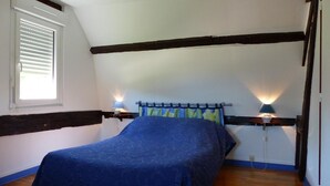 Un dormitorio con una cama, dos lámparas de noche, una ventana con persianas y un techo inclinado con vigas a la vista.