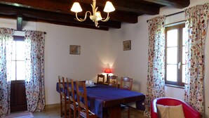 Un comedor con mesa de madera, sillas, una araña y cortinas con motivos florales.
