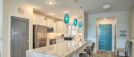 A modern kitchen with white cabinets, a large island, stainless steel appliances, and teal pendant lights.
