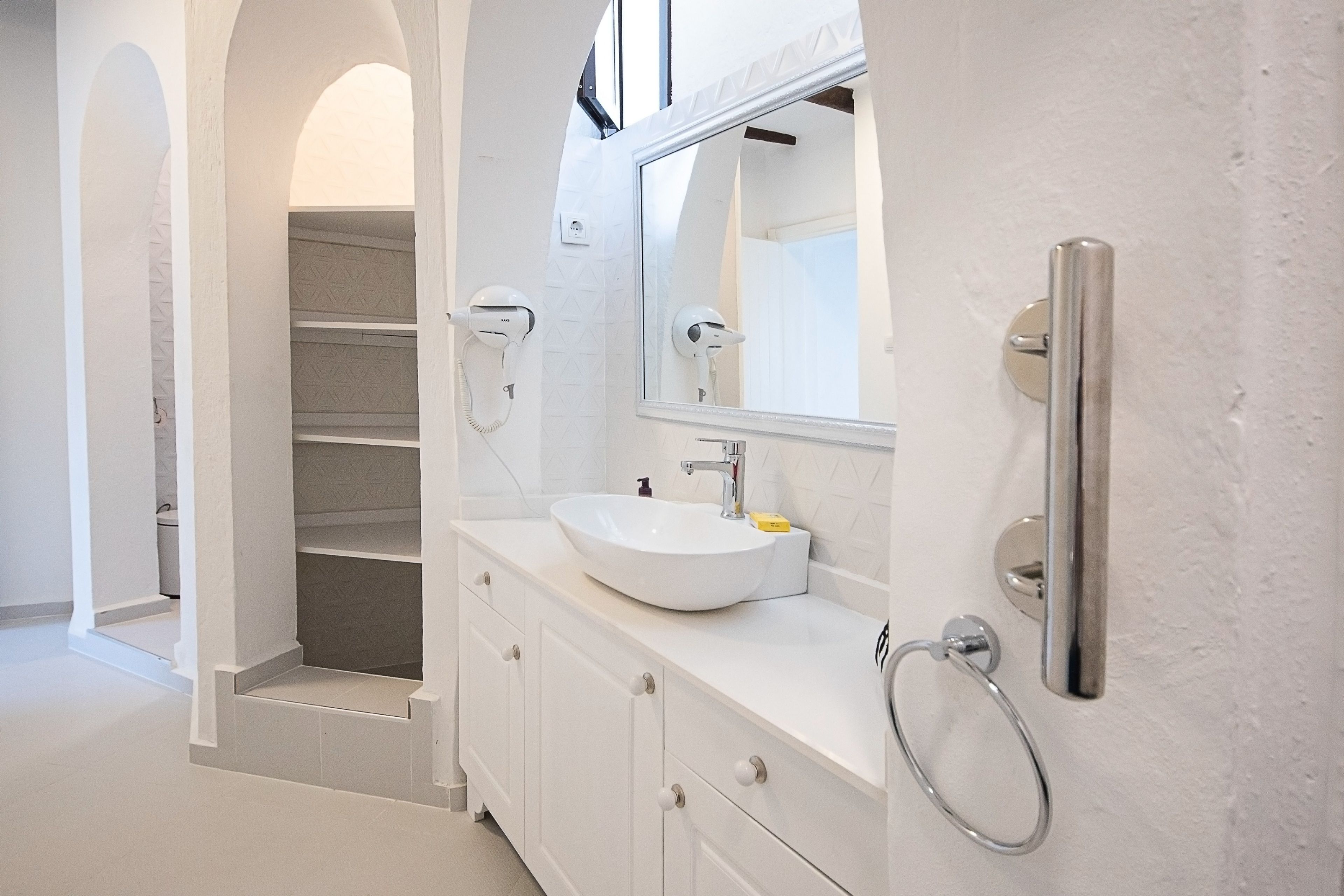 A modern bathroom with a white sink, a large mirror, and a towel rack.