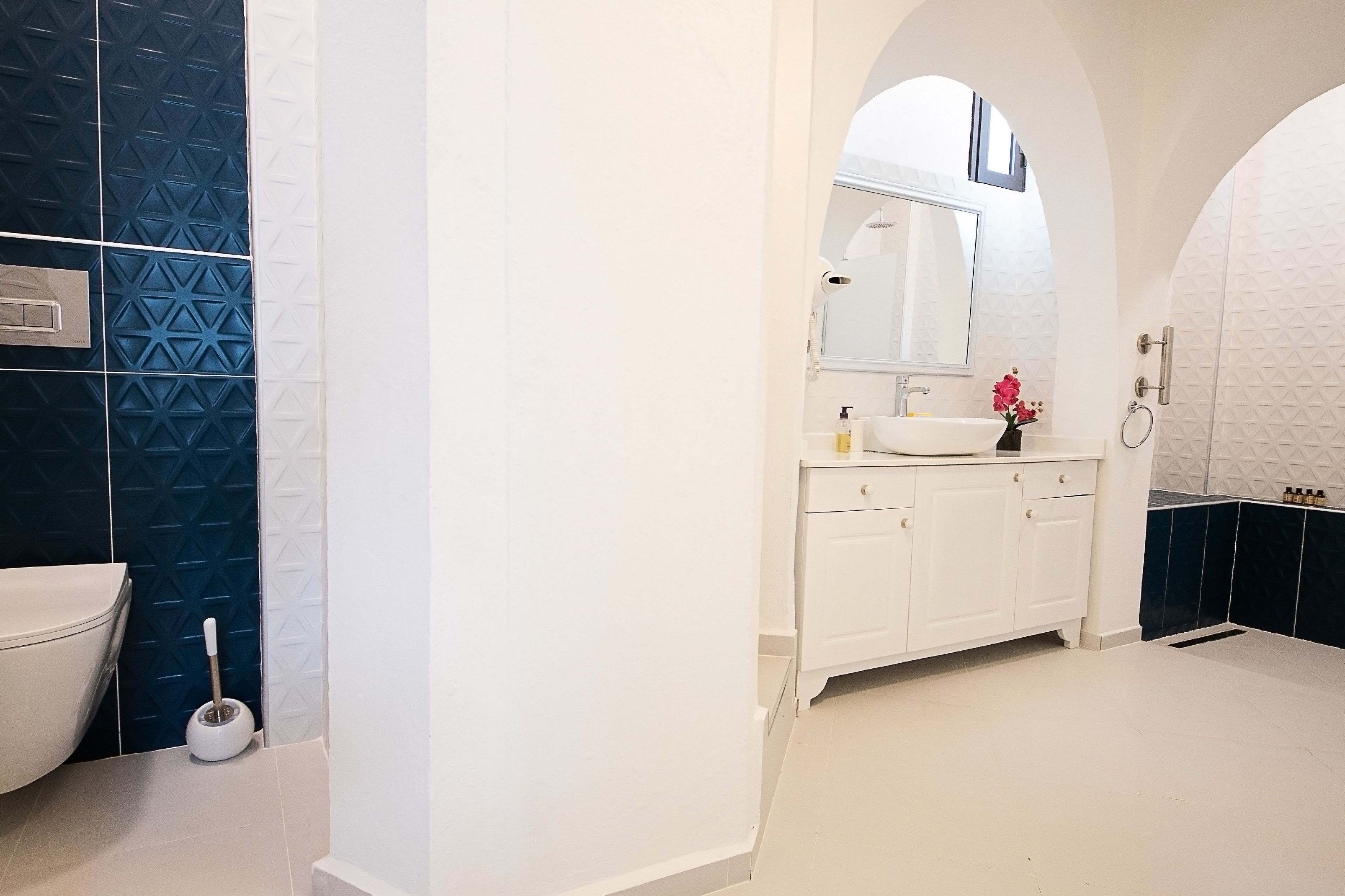 A modern bathroom with a white sink, mirror, and white cabinets.