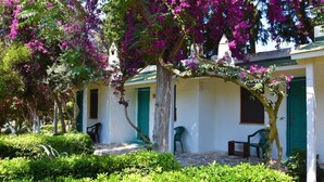 A building with a white exterior, green shutters, and a covered outdoor seating area with chairs. - Myndos Bed & Breakfast (Bodrum)