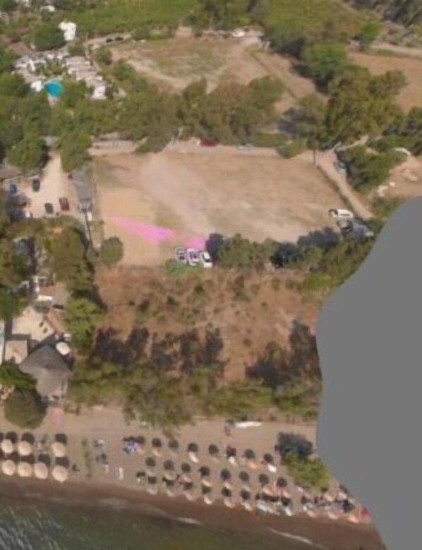 An aerial view of a coastal area with a beach, trees, and a few buildings.