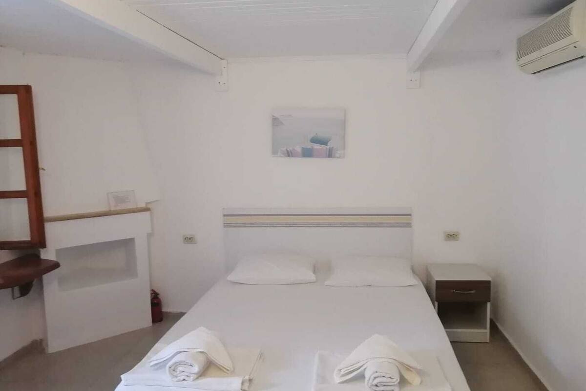 A small, clean room with a single bed, a nightstand, a small table, and a picture on the wall.