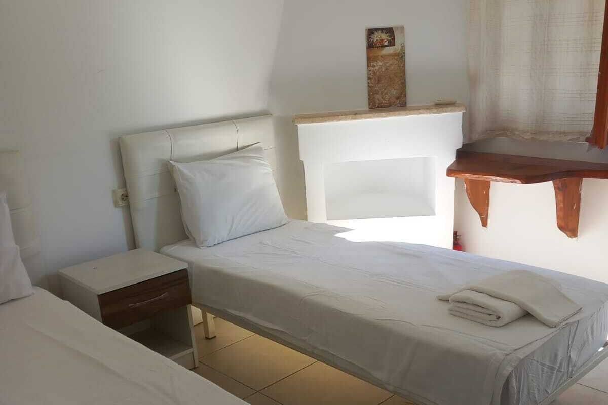 A bedroom with two beds, a nightstand, a wooden bench, and a window with curtains.