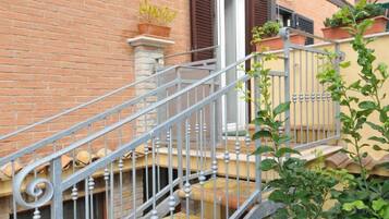 A brick building with a metal staircase leading to a door with a window. There are potted plants on the steps and a small balcony with railings.