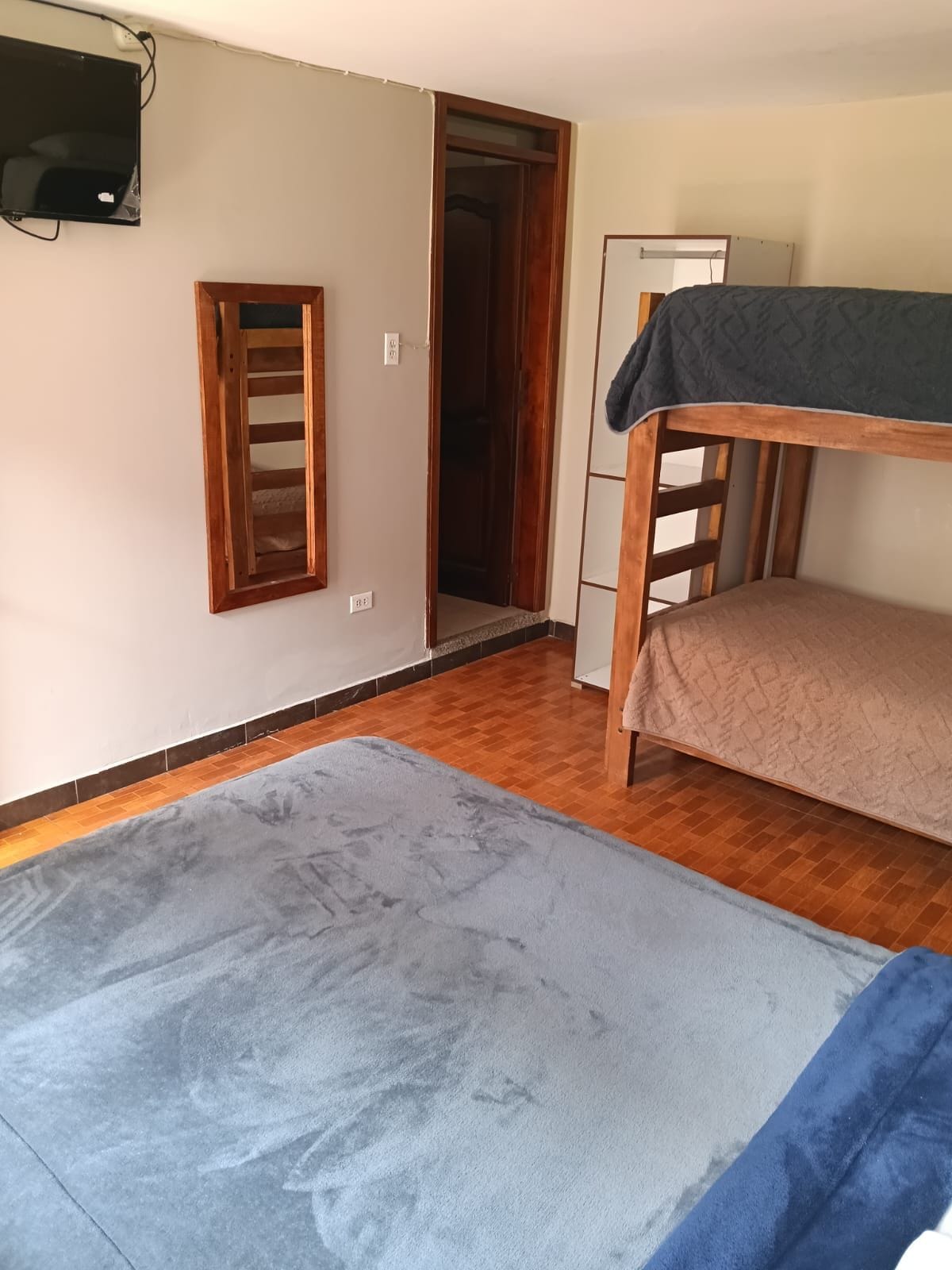 Una stanza con un letto a castello, una televisione fissata al muro e un'apertura che dà su un'altra stanza.
