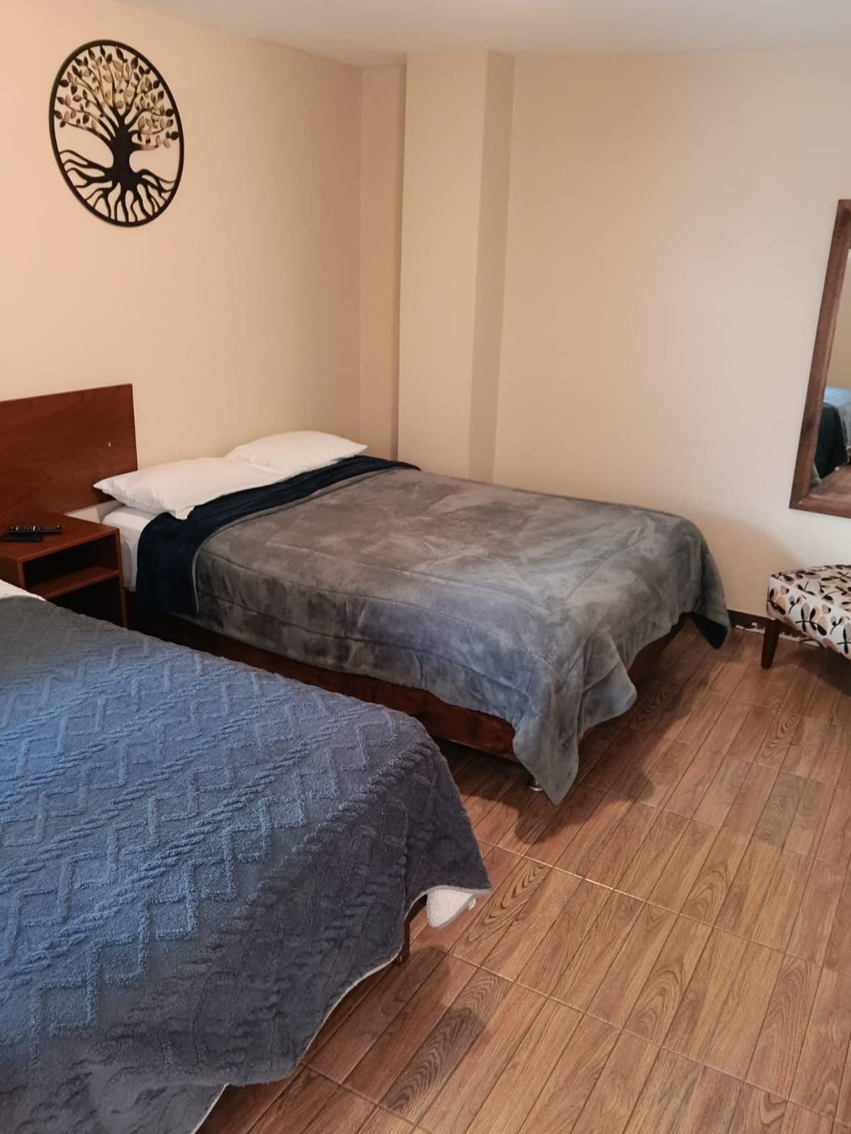 Una habitación con dos camas, cabecero de madera, un adorno de árbol en la pared, una mesita y un espejo.