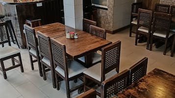 Un restaurante con mesas y sillas de madera, una zona de cocina y varias banderas colgando sobre la entrada.