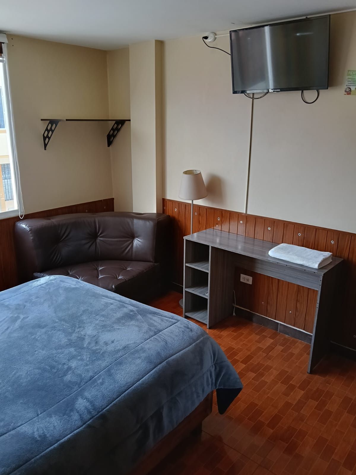 Una habitación de hotel con una cama, un escritorio, un televisor y una ventana.