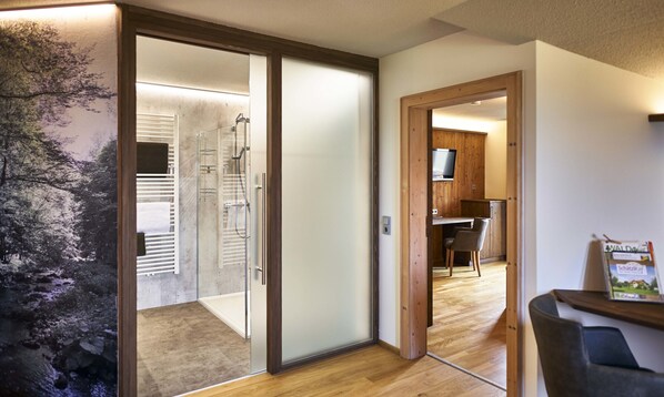 A modern bathroom with a glass shower enclosure, a wooden floor, and a view of a forest through the glass door. - Schätzlhof (Ruderting)
