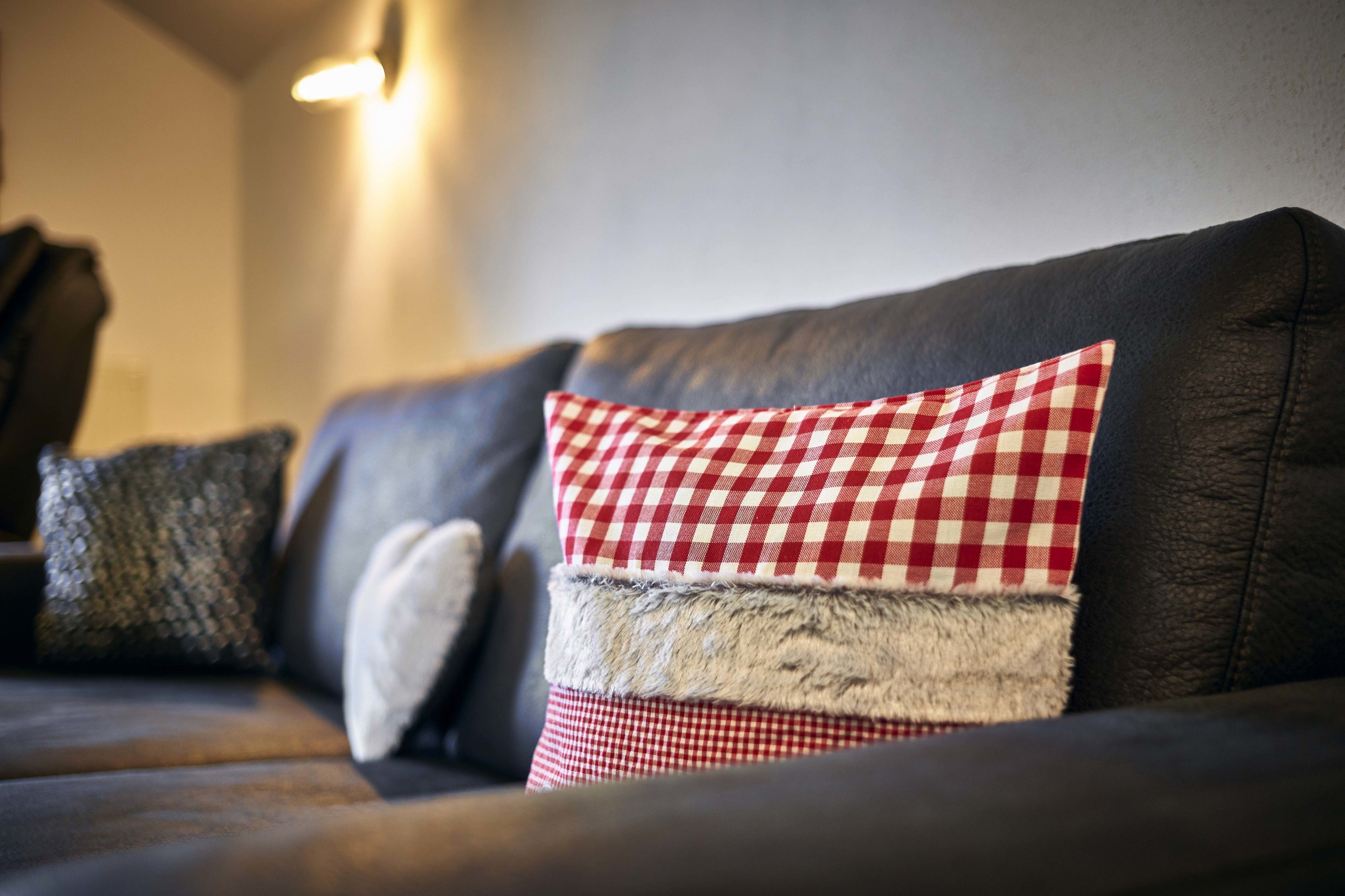 A dark leather sofa with three pillows, one with a red and white checkered pattern and another with a grey fur trim.