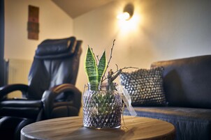 Un florero de vidrio con una planta sobre una mesa de madera en una sala de estar con un sillón de cuero y un cojín estampado.