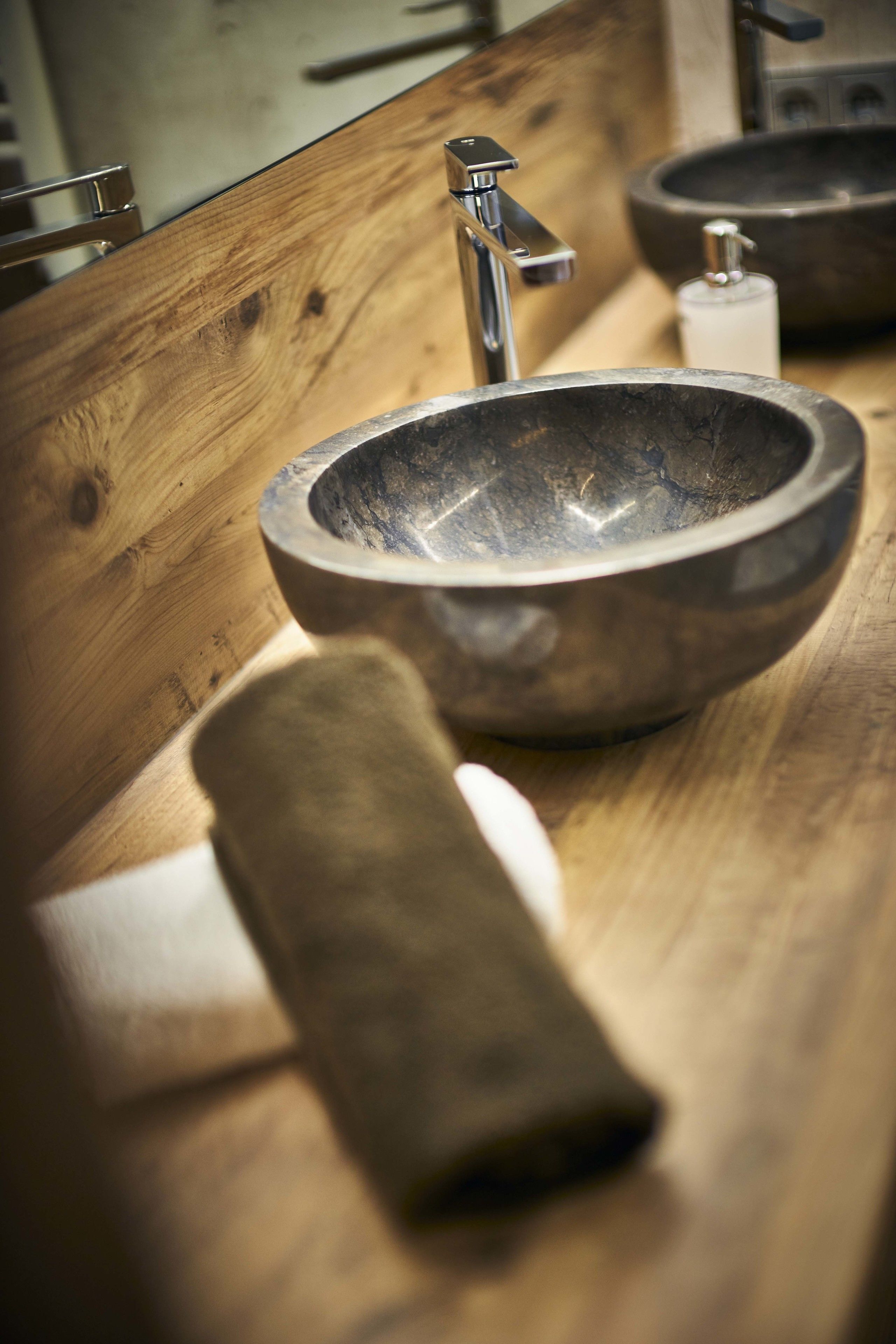 A wooden vanity with a stone sink, a modern faucet, and a soap dispenser.