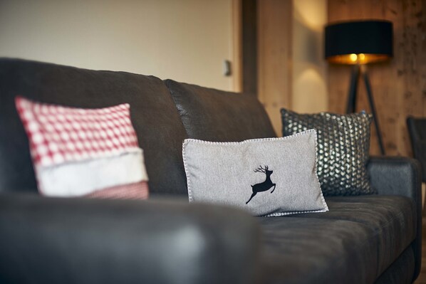 A dark brown leather sofa with three decorative pillows, one featuring a deer silhouette. - Schätzlhof (Ruderting)