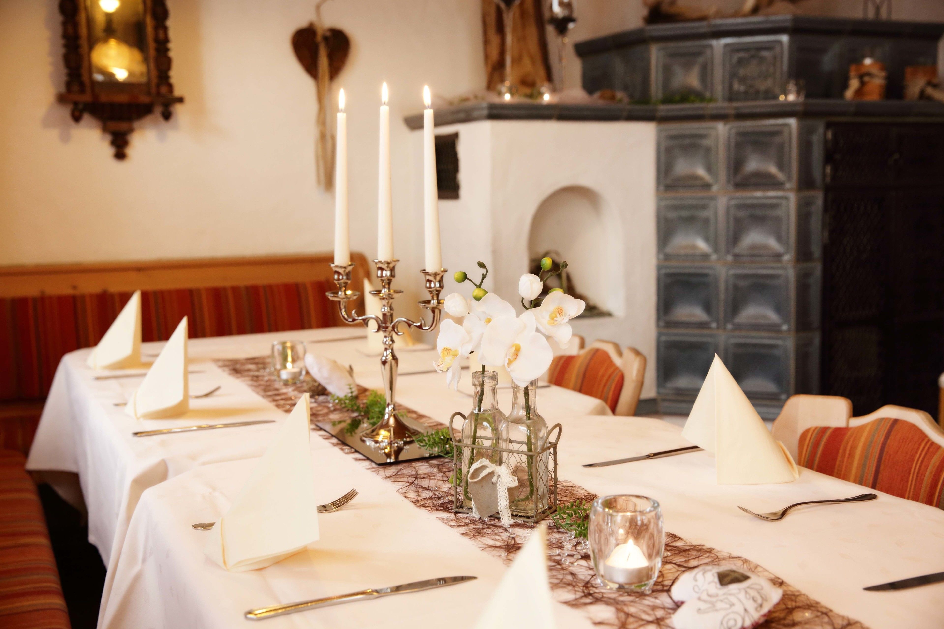 A dining table set with white tablecloths, candles, and orchid flowers.
