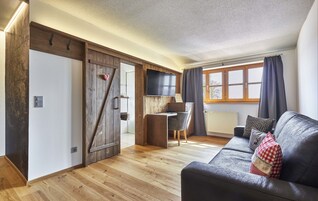 Una sala de estar moderna con piso de madera, un sofá de cuero negro, un escritorio de madera y un ventanal con cortinas.