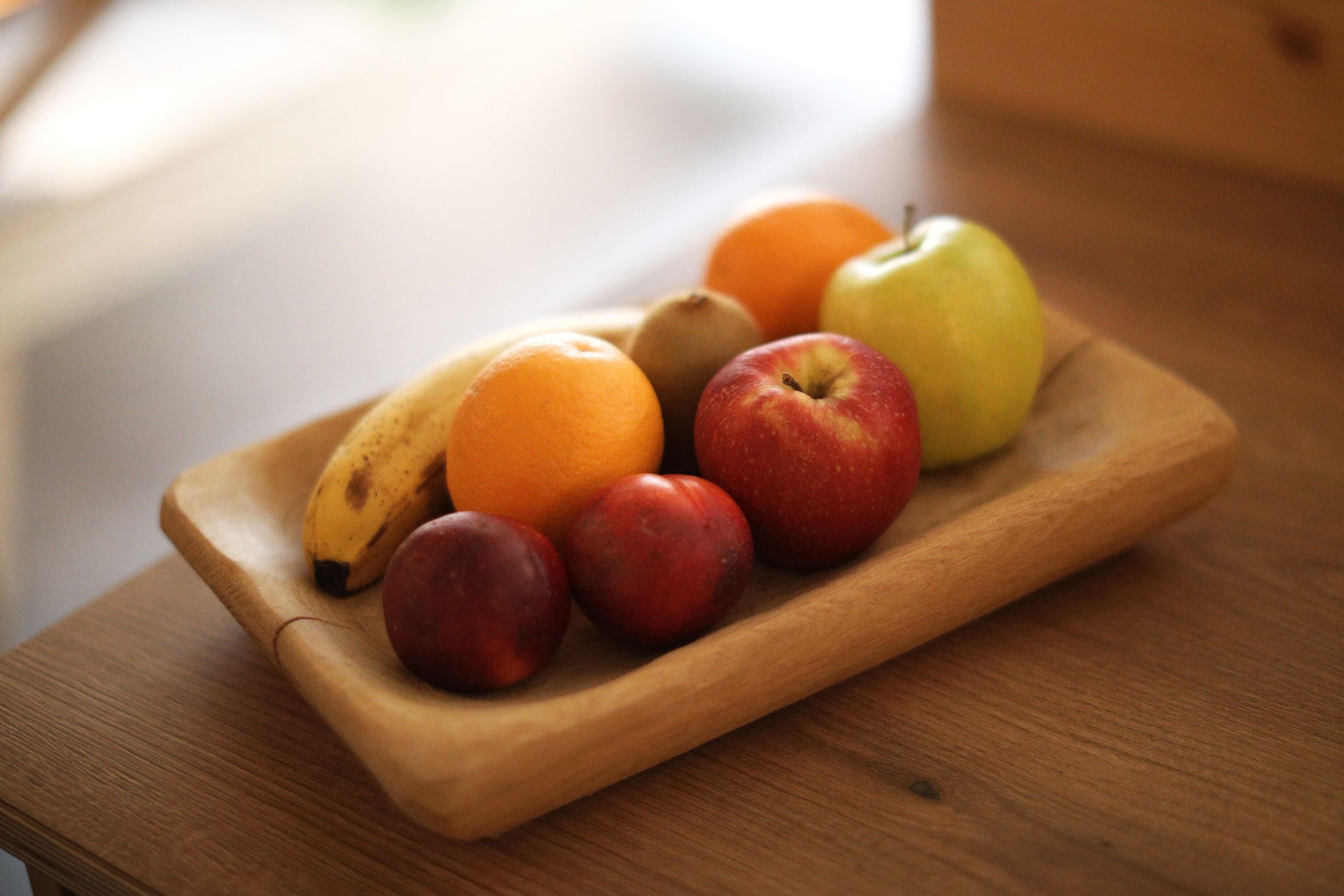 Een houten dienblad met verschillende soorten fruit, zoals appels, sinaasappels en bananen, op een tafel.