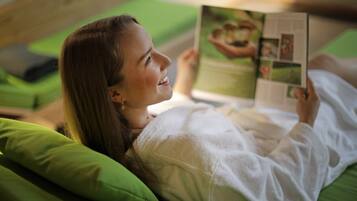 A person lying on a bed with green pillows, reading a magazine.