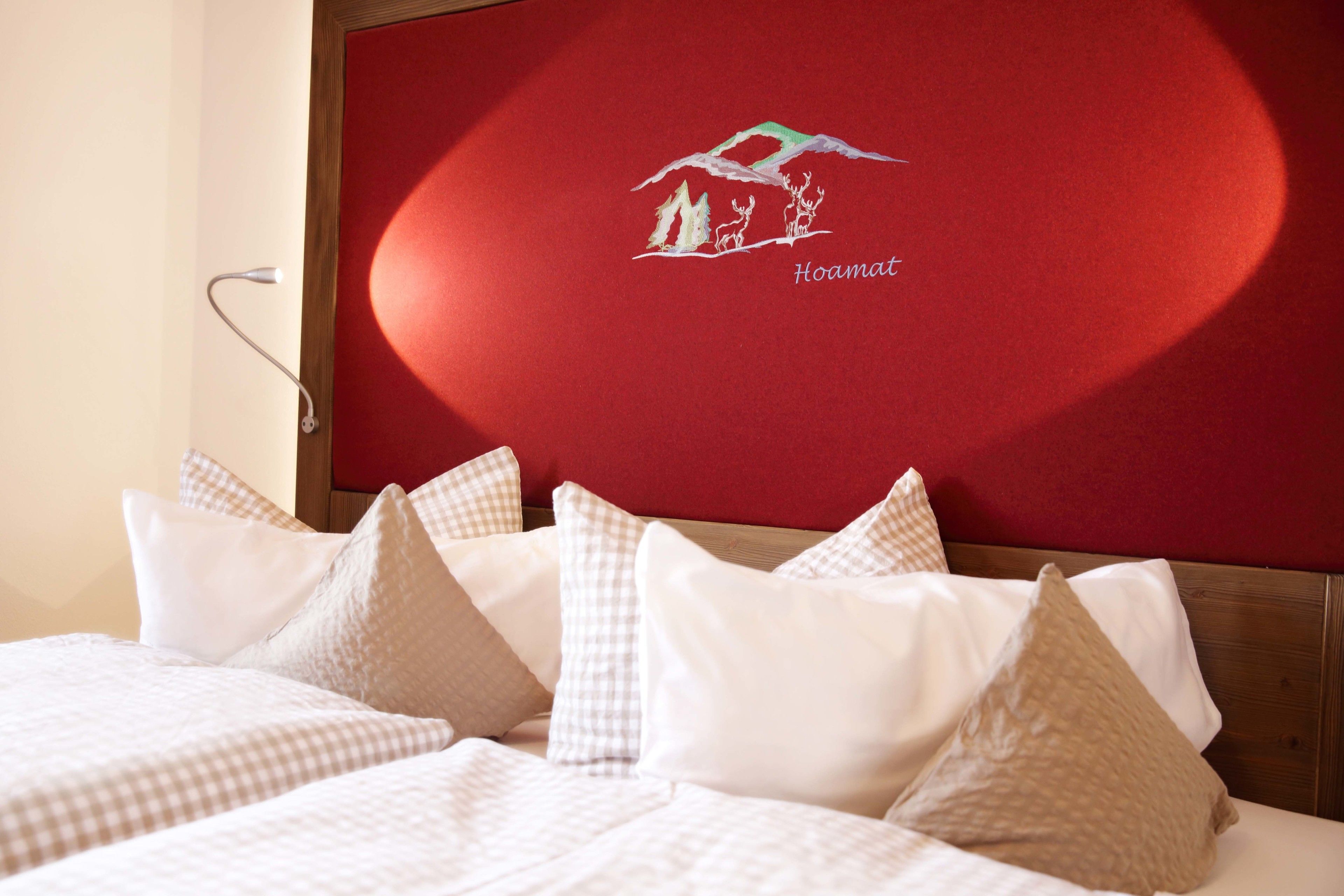 Una cama bien hecha con ropa de cama a cuadros y varias almohadas, un cabecero de madera y una pared roja con un gráfico y texto blancos.