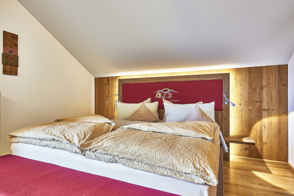 A bedroom with a wooden headboard, a red accent wall, and a bed with beige bedding.
