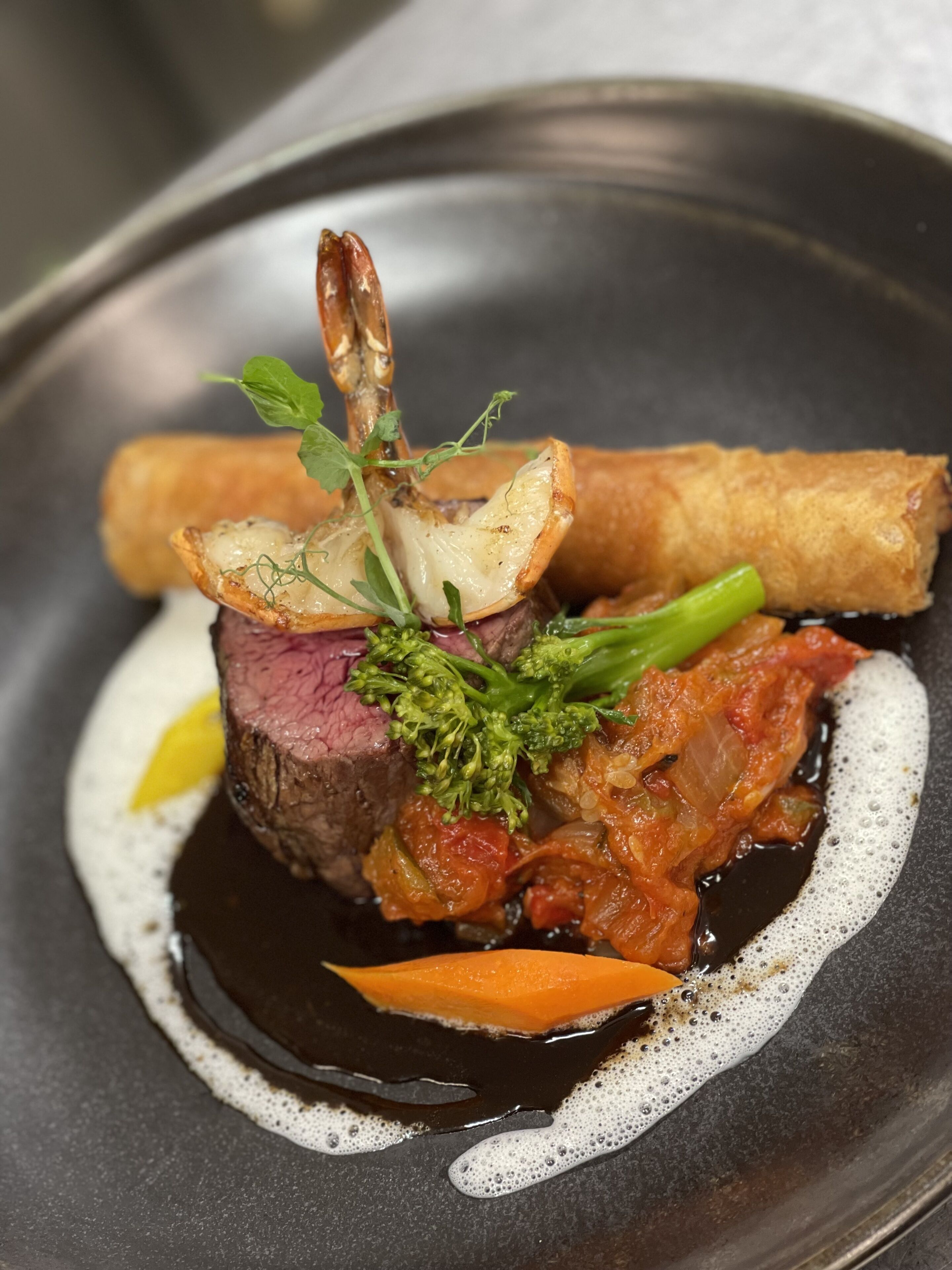A dish with a piece of meat, vegetables, and a sauce on a plate.