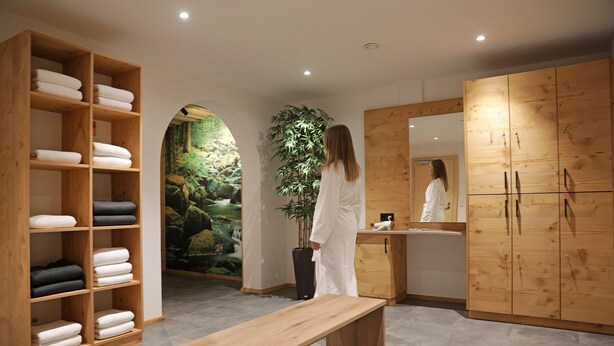 A spa room with wooden shelves holding towels, a bench, a large mirror, and a potted plant. - Schätzlhof (Ruderting)