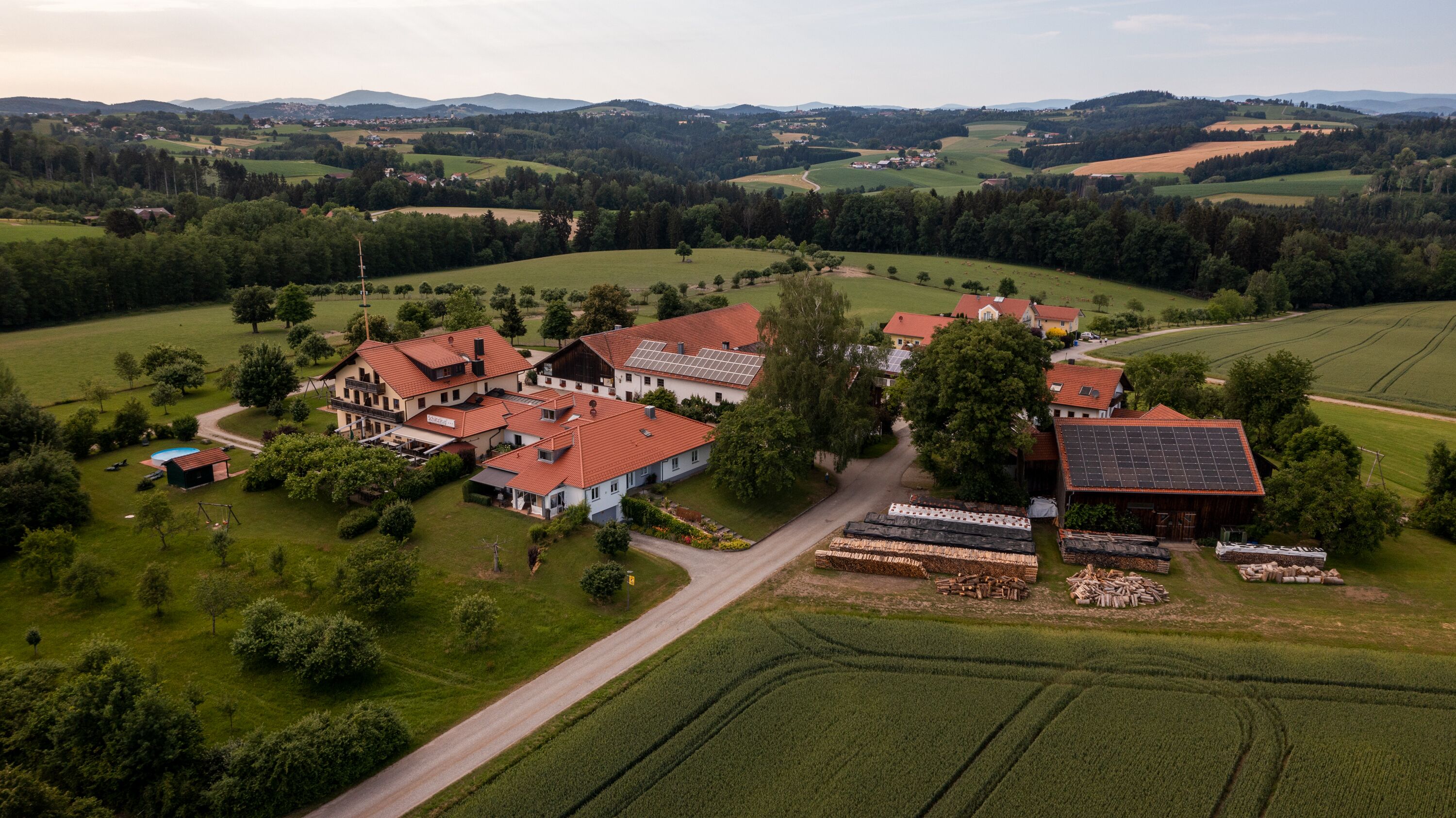 Vista aérea de una propiedad rural con varias construcciones, incluyendo una casa grande de techo rojo y paneles solares, rodeada de campos y árboles.
