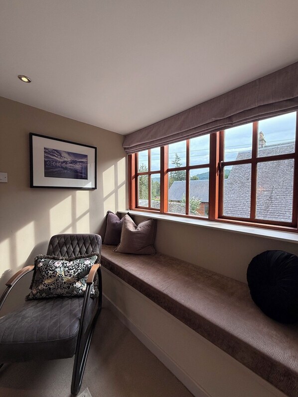 A room with a built-in bench along a large window, a framed picture on the wall, and a chair with a cushion. - Craigatin House & Courtyard (Adults only) (Pitlochry)