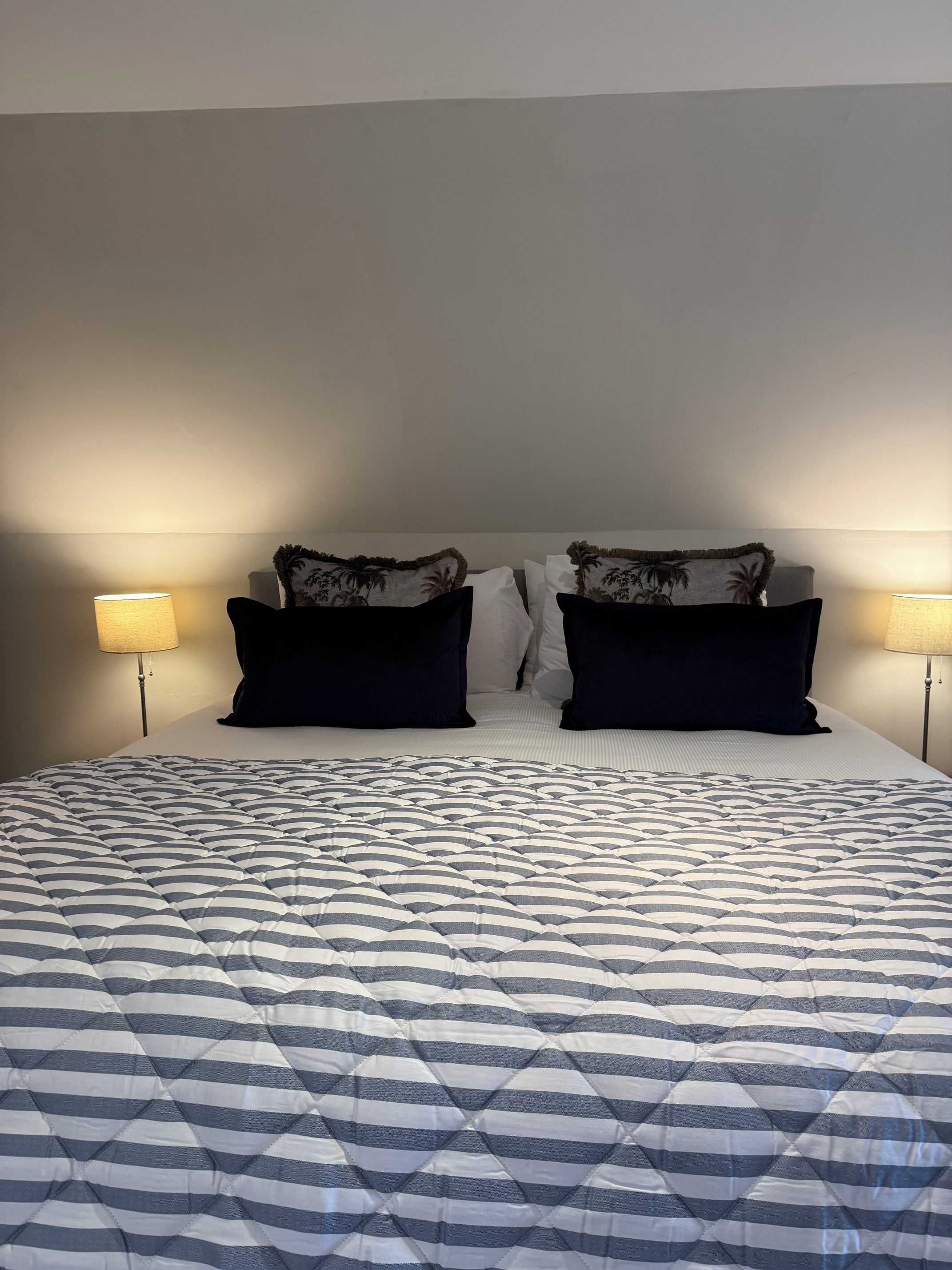 A bed with a striped quilt, two black pillows, and a headboard against a plain wall.