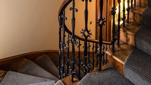 A wooden staircase with ornate black metal railings and a light fixture on the wall. - Craigatin House & Courtyard (Adults only) (Pitlochry)
