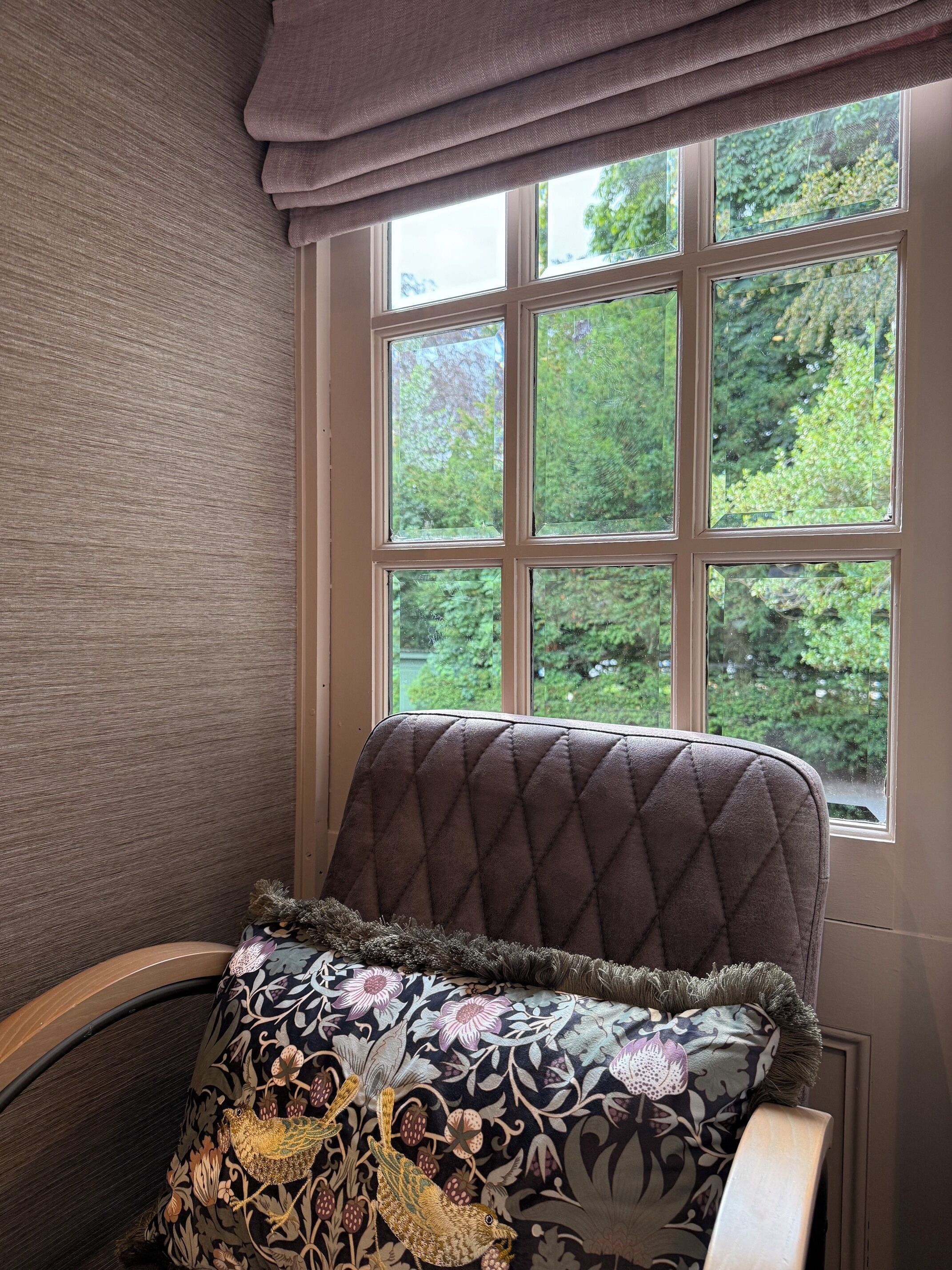 A room with a window, a chair, and a patterned pillow.