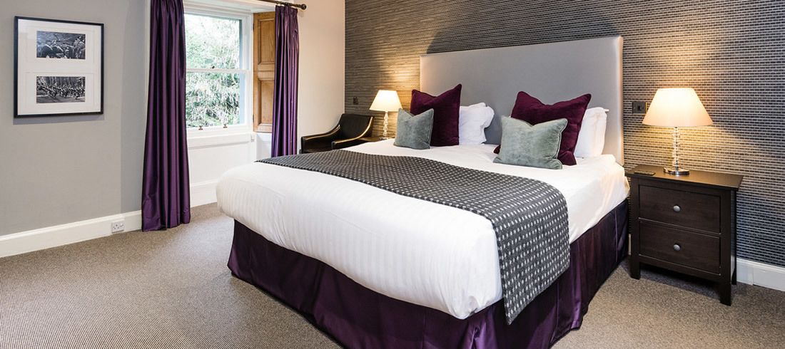 A neatly arranged hotel room with a large bed, two bedside tables, and a window with curtains.