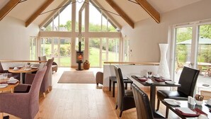 A dining area with multiple tables and chairs, a fireplace, and large windows offering a view of the outdoors. - Craigatin House & Courtyard (Adults only) (Pitlochry)
