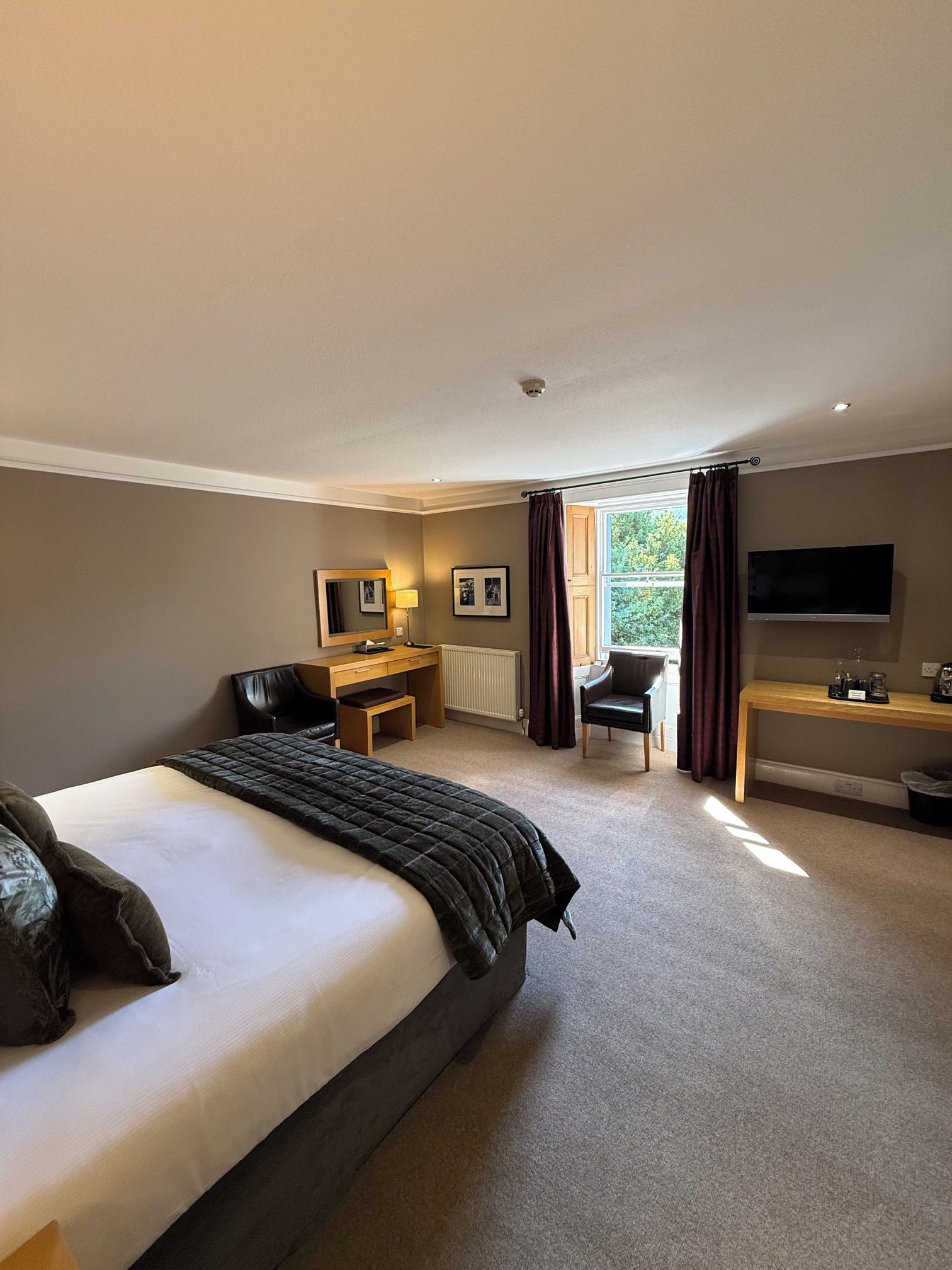A hotel room with a large bed, a desk, a chair, a television, and a window with curtains.
