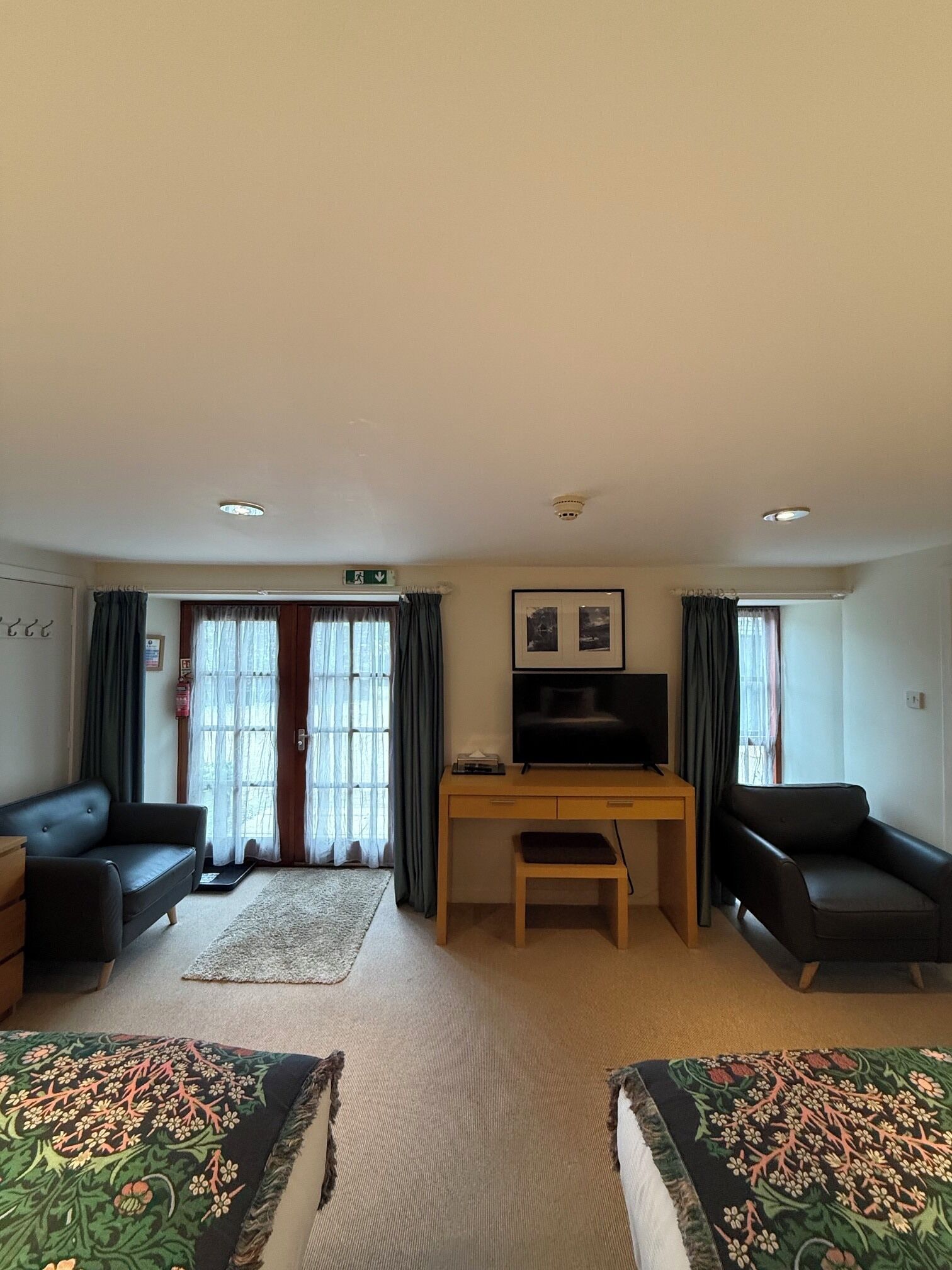 A room with a bed, a desk, a chair, a television, and a window with curtains.