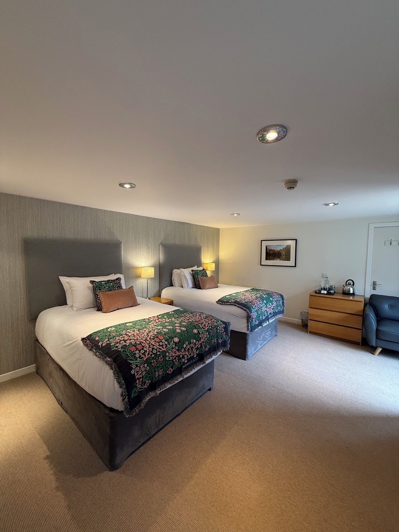 Une chambre d’hôtel avec deux lits, une commode, une chaise et un tableau encadré au mur.