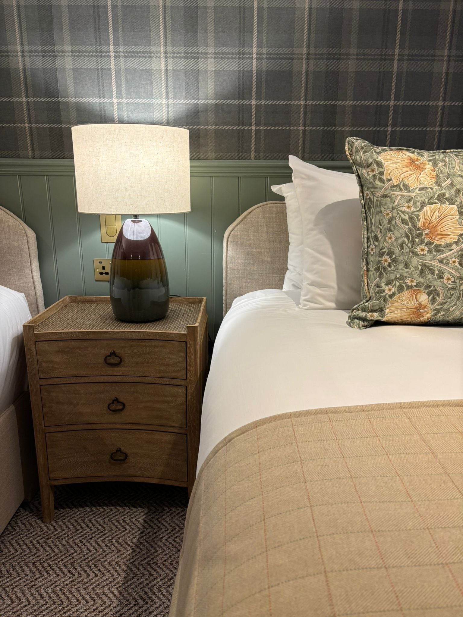 A neatly made bed with a floral pillow, a bedside lamp, and a wooden nightstand with drawers.
