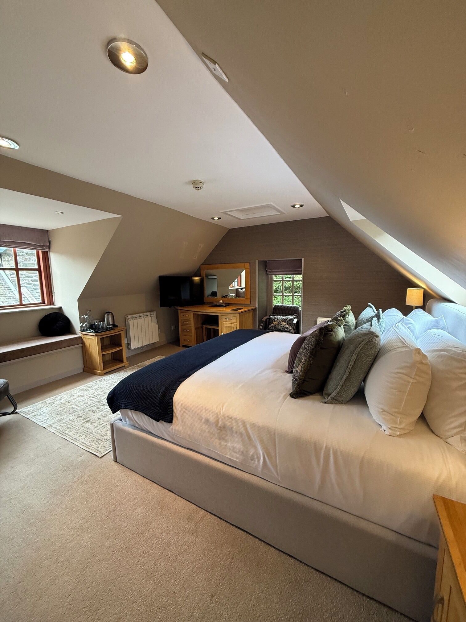 Ein Schlafzimmer mit einem großen Bett, einem Schreibtisch, einem Sessel, einem Fernseher und einem Fenster.