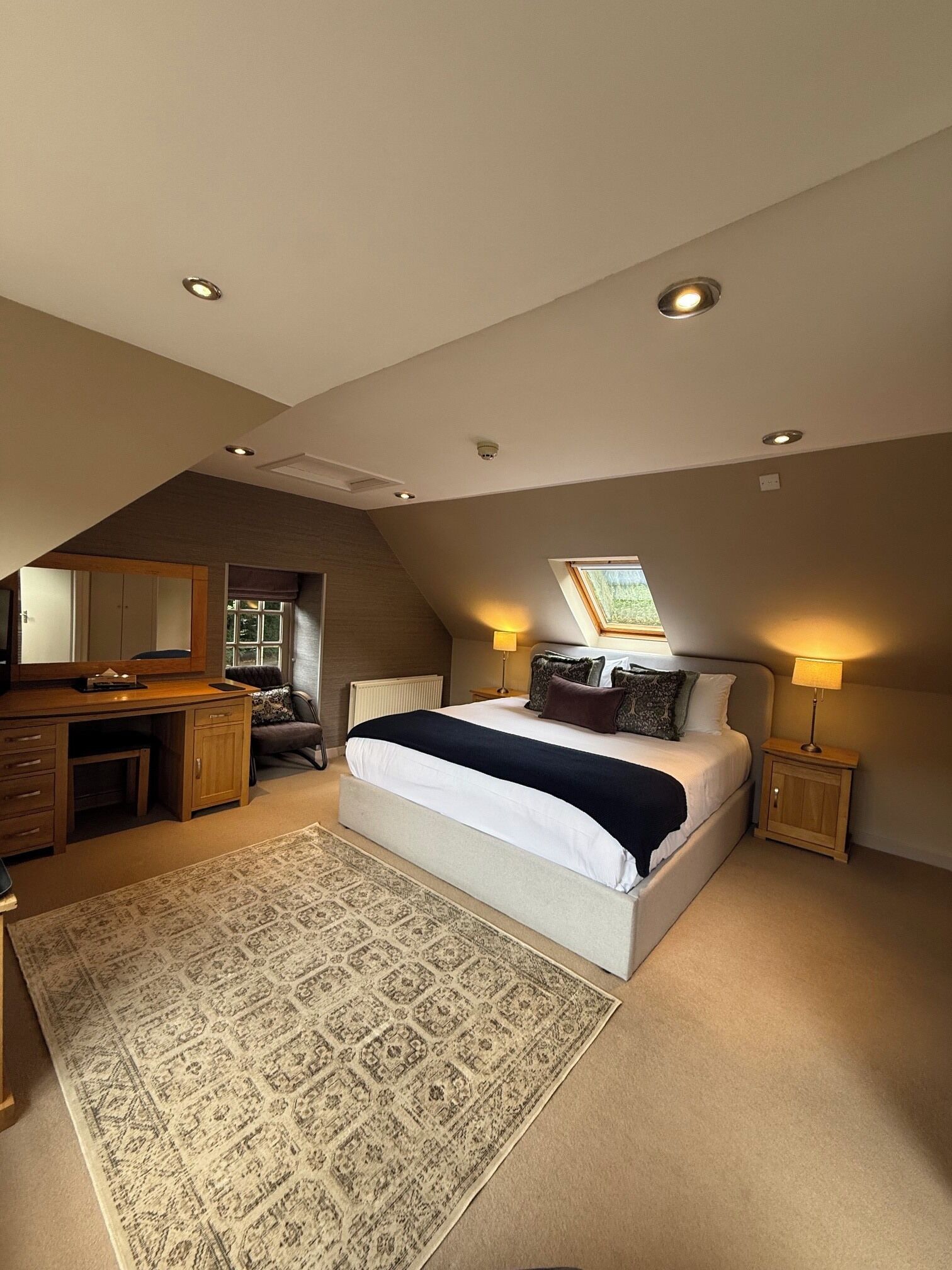 A bedroom with a large bed, a desk, a chair, a window, and a skylight.