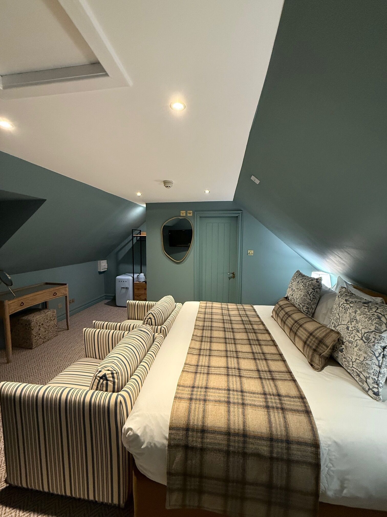 A bedroom with a bed, a sofa, a desk, and a mirror.