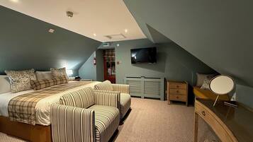 Un dormitorio con una cama, dos sillones a rayas, un aparador, un espejo y un televisor en la pared.